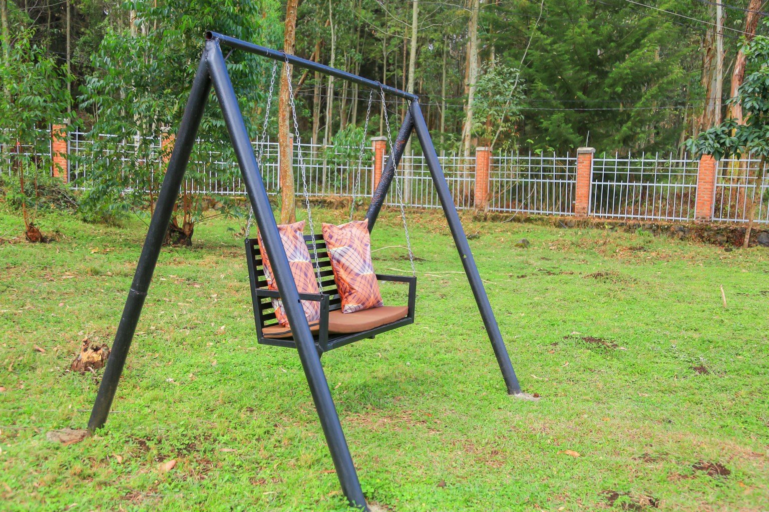 Black metal garden swing on a lawn beneath tall trees