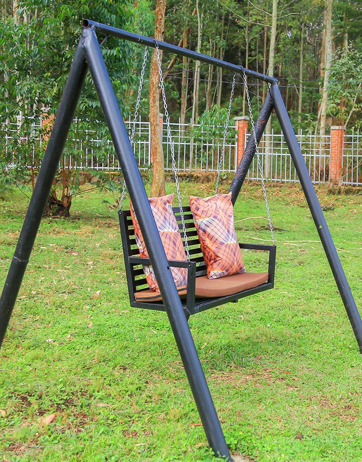 Garden swing on the lawn with a white fence and tall trees behind
