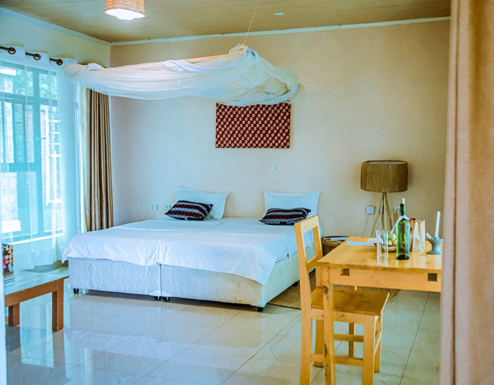 African-style double room with white bedding, woven pillows and a patterned wall hanging