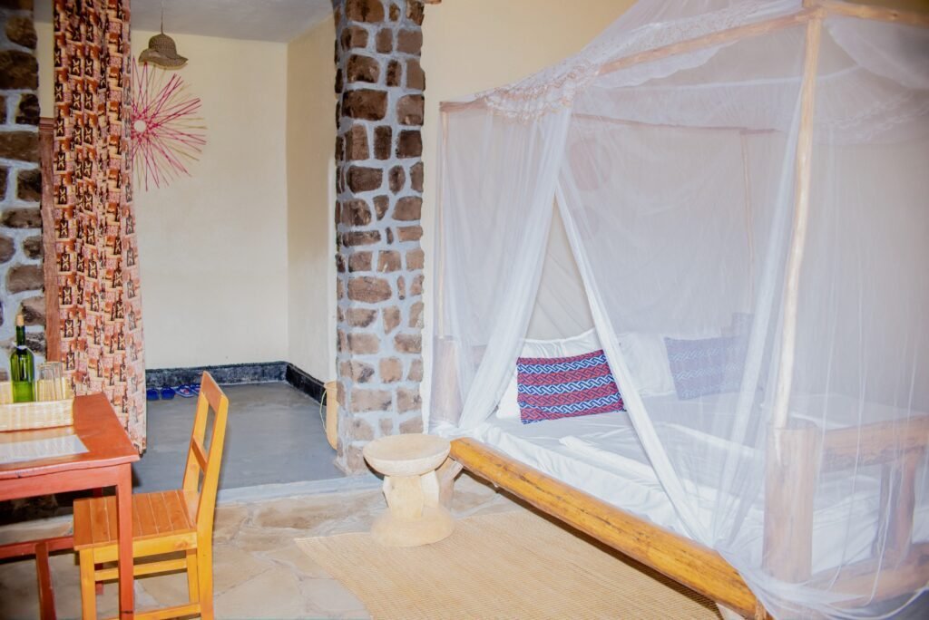 African-style room with a stone feature wall, four-poster bed draped in white netting and woven textiles
